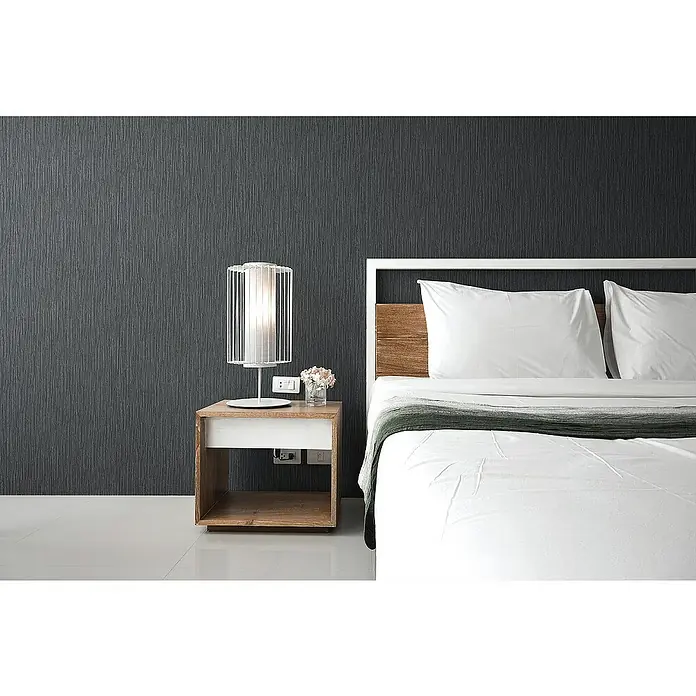 Tadessi Vliestapete M1-No.1119 - Schwarz, Uni, 10,05 x 0,53 m - Moderner Holznachttisch mit weißer Schublade neben einem Bett, darauf eine weiße Gittertischlampe.