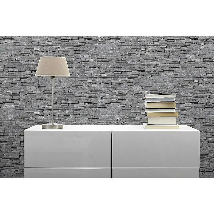 Tadessi Vliestapete M1-No.4322 - Grau, Steinoptik, 10,05 x 0,53 m - Graue Steinoptik-Tapete an einer Wand hinter einem weißen Schrank mit Lampe und Büchern.