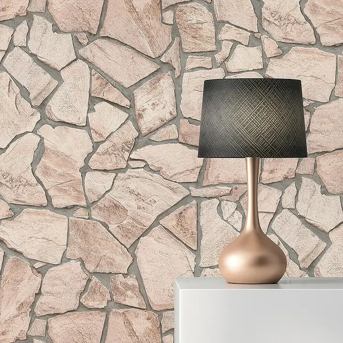 Tadessi Vliestapete M1-No.3693 - Grau, Steinoptik, 10,05 x 0,53 m - Roségoldene Tischlampe mit dunklem Musterschirm auf einer weißen Oberfläche vor einer Steinwand.