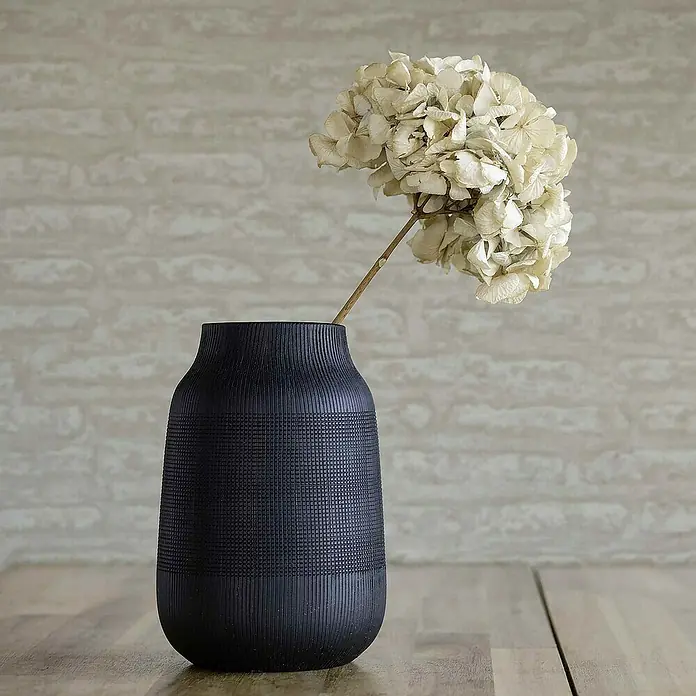 Tadessi Vliestapete M1-No.4191 - Braun, Steinoptik, 10,05 x 0,53 m - Dunkelblaue strukturierte Vase mit Gitter- und Vertikalmustern, die eine getrocknete cremefarbene Hortensie hält. Auf einer Holzfläche platziert.