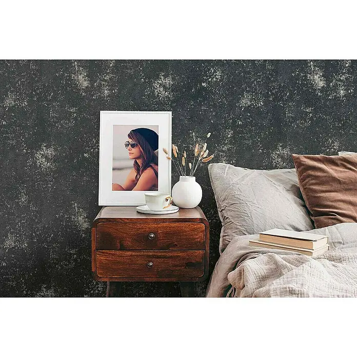 Tadessi Vliestapete M1-No.4075 - Schwarz, Sonstiges, 10,05 x 0,53 m - Dunkle, texturierte Tapete mit Distressed-Effekt bedeckt eine Schlafzimmerwand hinter Nachttisch und Bett.