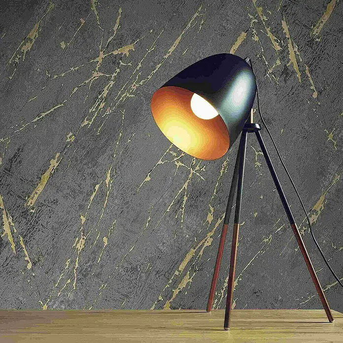 Tadessi Vliestapete M1-No.4012 - Gold, Steinoptik, 10,05 x 0,53 m - Schwarze Dreibeinlampe mit goldener Innenseite, die ein warmes Licht abgibt, auf einer Holzfläche stehend.