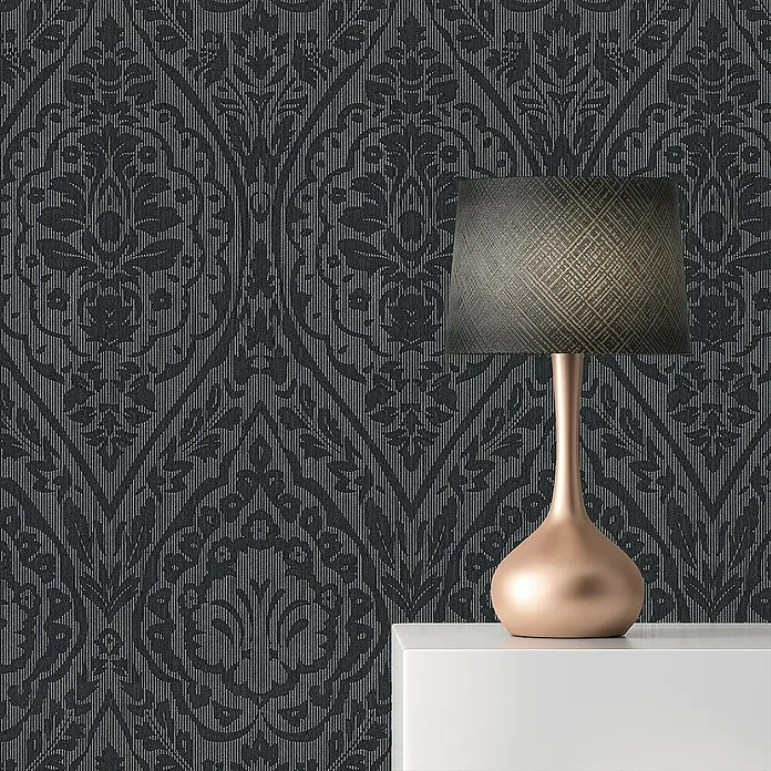 Tadessi Vliestapete M1-No.3857 - Schwarz, Streifen, 10,05 x 0,53 m - Dunkle Tapete mit Damastmuster an einer Wand, davor eine bronzefarbene Lampe auf einem weißen Tisch.