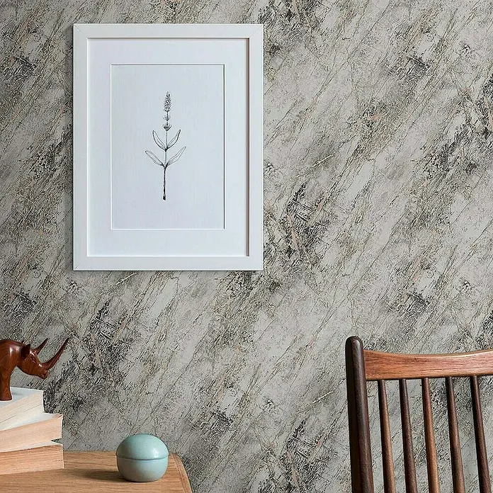 Tadessi Vliestapete M1-No.4011 - Schwarz, Steinoptik, 10,05 x 0,53 m - Marmor-Effekt-Tapete mit grauen, schwarzen und roségoldenen Maserungen, schmückt eine Wand hinter einem gerahmten Pflanzendruck und Holzmöbeln.