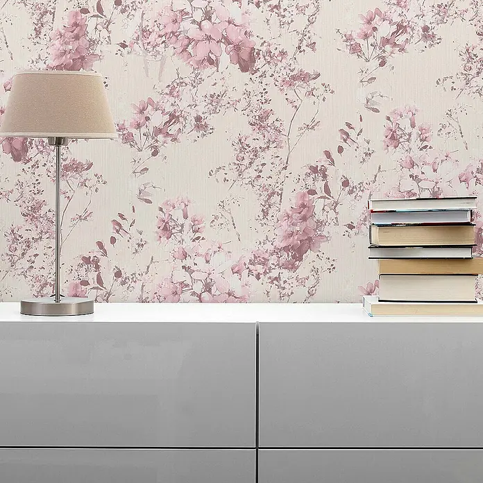 Tadessi Vliestapete M1-No.1301 - Rosa, Floral - Rosa Blumenmuster-Tapete ziert eine Wand hinter einem hellgrauen Schrank mit Lampe und Büchern.