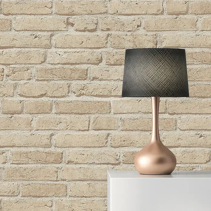 Tadessi Vliestapete M1-No.2593 - Beige, Steinoptik, 10,05 x 0,53 m - Roségoldene Tischlampe mit dunklem, gemustertem Schirm auf einem weißen Regal vor einer Ziegelwand.