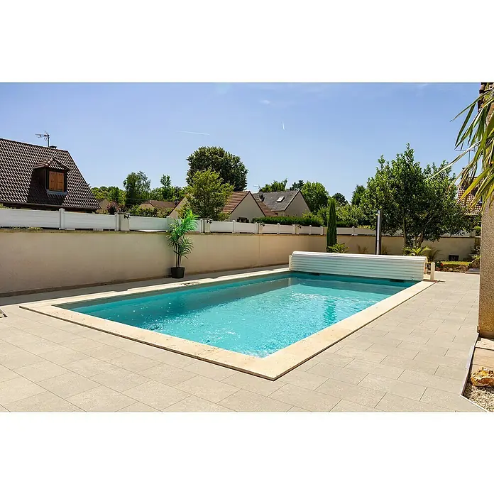 EHL Terrassenplatte Mantina - 60 x 40 x 4 cm, Greige, Beton - Außenaufnahme eines rechteckigen Schwimmbeckens mit aufgerollter Abdeckung, umgeben von Terrassenfliesen und einer Mauer mit Dekoration.