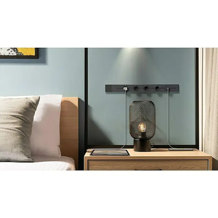 Schwaiger USB-Steckdose Adapter USB-A, USB-C - 6,2 cm, Schwarz - Das graue Wandsteckdosenleiste-Design mit USB-Anschlüssen ist an der Wand befestigt und lädt Geräte auf einem Nachttisch mit einer Lampe auf.