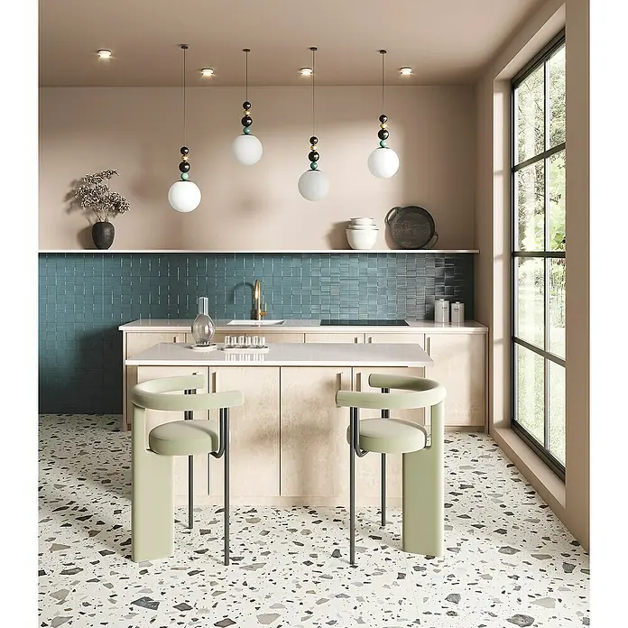 Feinsteinzeugfliese Pebble - 59,55 x 59,55 cm, Ivory, Matt - Elegante Küchenansicht mit modernen Pendelleuchten über einer Kochinsel und stilvollen, grünen Barhockern vor einer blauen Wand.