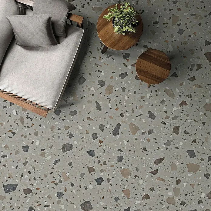 Feinsteinzeugfliese Pebble - 59,55 x 59,55 cm, Grey, Matt - Ansicht von oben: Terrazzobodenfliesen mit Couch, kleinem Tisch und Pflanze. Moderne und stilvolle Bodenlösung für den Innenbereich.