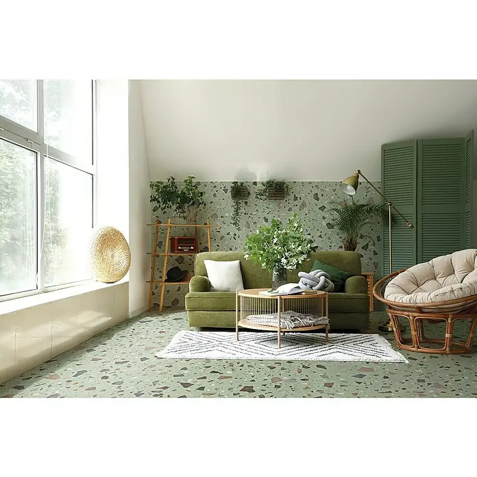 Feinsteinzeugfliese Pebble - 59,55 x 59,55 cm, Green, Matt - Wohnzimmer mit grünem Sofa, rundem Rattansessel und Couchtisch auf einem geometrischen Teppich. Dekorative Elemente wie Pflanzen und eine Stehlampe vervollständigen den Raum.