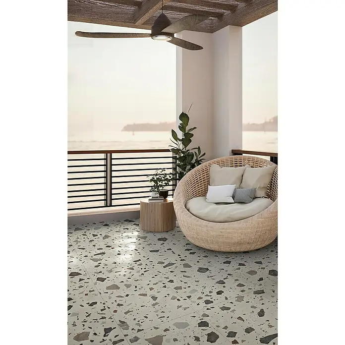 Feinsteinzeugfliese Pebble - 59,55 x 59,55 cm, Ivory, Matt - Terrasse mit Terrazzoboden und Rattan-Sessel. Die Outdoor-Fliesen in Terrazzo-Optik verleihen dem Balkon ein modernes Flair.