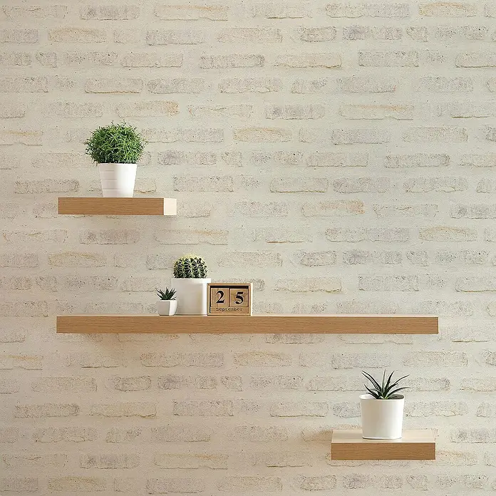 Tadessi Vliestapete M1-No.417 - Grau, Steinoptik, 10,05 x 0,53 m - Drei schwebende Regale aus hellem Holz mit Pflanzen und Kalender an einer Ziegelwand.