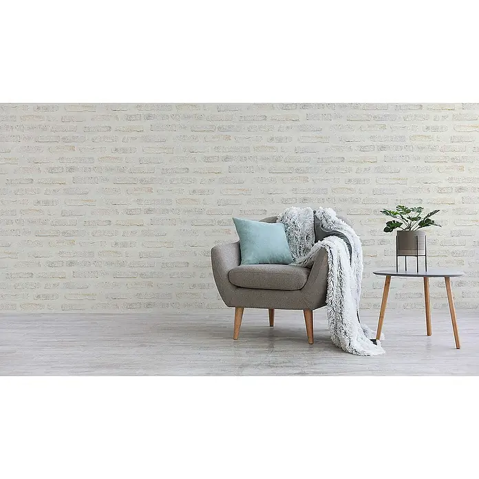 Tadessi Vliestapete M1-No.417 - Grau, Steinoptik, 10,05 x 0,53 m - Ein gemütlicher grauer Sessel mit blauem Kissen und flauschiger Decke, neben einem grauen Beistelltisch mit Pflanze.