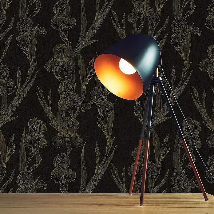 Tadessi Vliestapete M1-No.1376 - Schwarz, Floral, 10,05 x 0,53 m - Schwarze Stativ-Tischlampe mit kupferfarbener Innenseite, leuchtet eine dunkel gemusterte Wand von einem Holztisch aus.