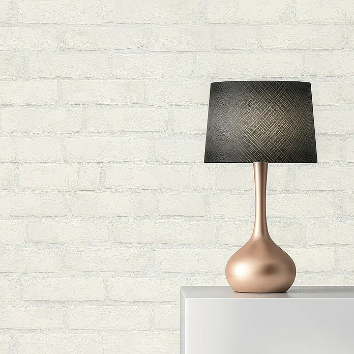 Tadessi Vliestapete M1-No.870 - Weiß, Steinoptik, 10,05 x 0,53 m - Eine moderne Tischlampe mit kupferfarbenem Fuß und dunklem Lampenschirm auf einer weißen Oberfläche vor einer hellen Ziegelwand.