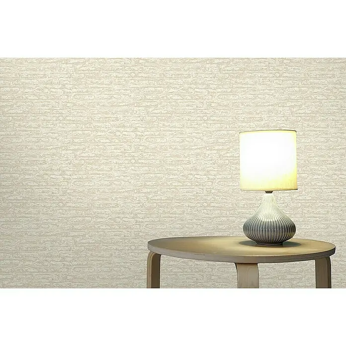 Tadessi Vliestapete M1-No.4192 - Weiß, Steinoptik, 10,05 x 0,53 m - Helle, strukturierte Tapete mit subtilem Ziegelmuster an einer Wand, als Hintergrund für einen Tisch und eine Lampe.