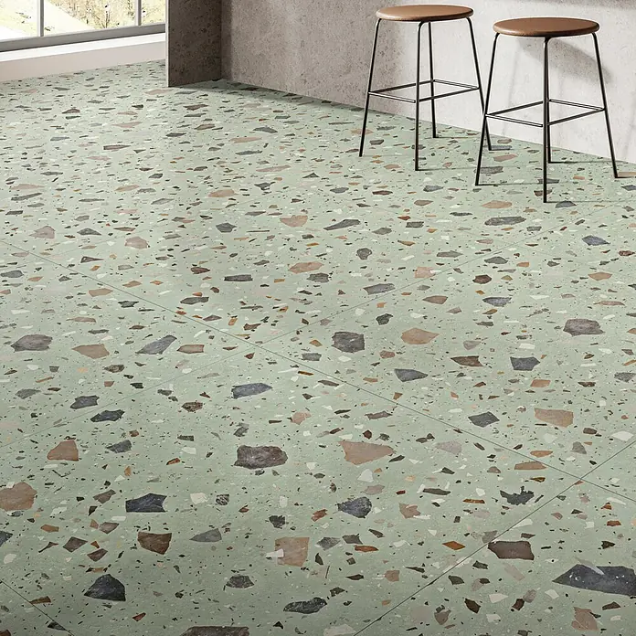 Feinsteinzeugfliese Pebble - 59,55 x 59,55 cm, Green, Matt - Detailaufnahme eines Bodens mit Terrazzo-Optik und zwei Hockern im Hintergrund.