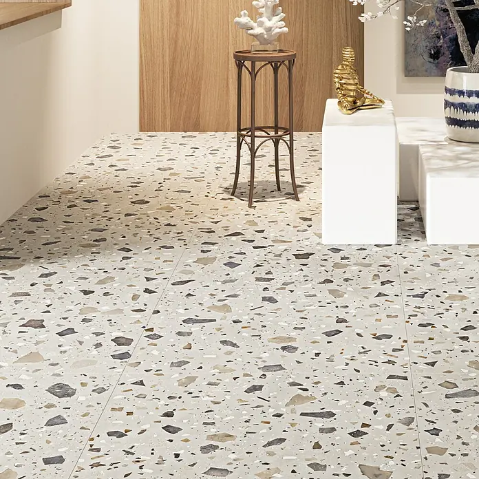 Feinsteinzeugfliese Pebble - 59,55 x 59,55 cm, Ivory, Matt - Nahaufnahme von Terrazzoplatten in einem Innenraum mit dekorativen Elementen und einem kleinen Tisch. Die Terrazzo Fliesen sind in hellen Farbtönen gehalten.