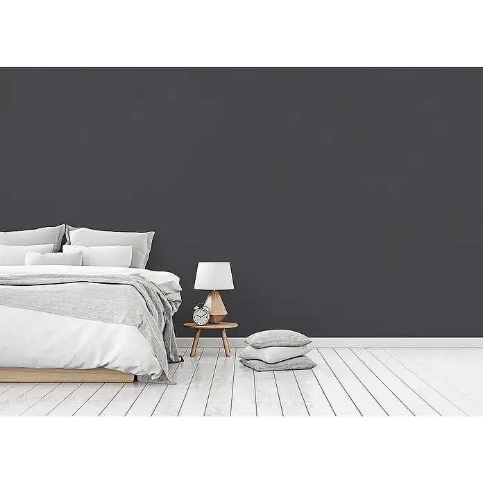 Tadessi Vliestapete M1-No.1906 - Schwarz, Uni, 10,05 x 0,53 m - Eine dunkelgraue Wand dient als moderne Kulisse in einem Schlafzimmer mit weißen Bettwaren und einem Nachttisch aus Holz.