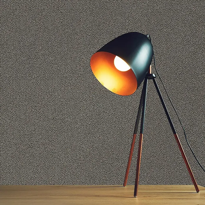 Tadessi Vliestapete M1-No.2869 - Schwarz, Sonstiges, 10,05 x 0,53 m - Schwarze Tischlampe mit Kupfer-Innenseite und dunklen Beinen, beleuchtet auf einem Holztisch vor gemusterter Wand.