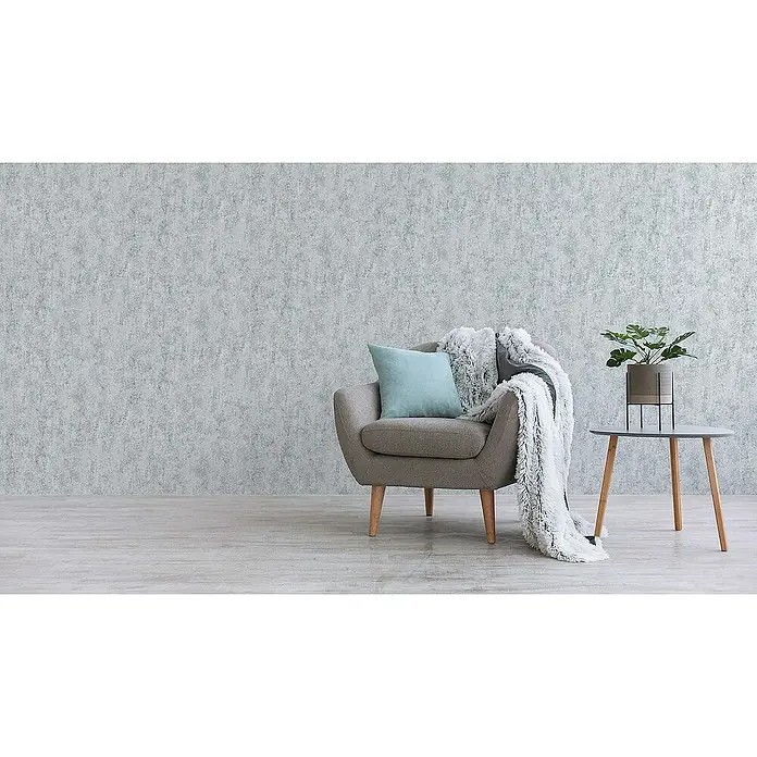 Tadessi Vliestapete M1-No.163 - Grau, Steinoptik, 10,05 x 0,53 m - Bequemer grauer Sessel mit hellblauem Kissen und flauschiger weißer Decke in einem modernen Wohnbereich.