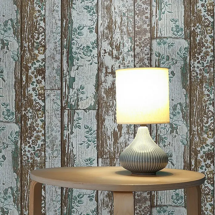 Tadessi Vliestapete M1-No.1628 - Braun, Holzoptik, 10,05 x 0,53 m - Eine Tischlampe mit hellem Schirm und geripptem grauem Fuß steht auf einem runden Holztisch.