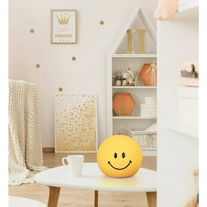 FHL easy LED-Nachtlicht GlowMoji - 0,3 W, L x B x H: 13 x 13 x 12 cm, Warmweiß, Smiley Yellow - Runde, gelbe Tischleuchte mit lächelndem Gesicht. Die Lampe steht auf einem kleinen Tisch im Kinderzimmer.