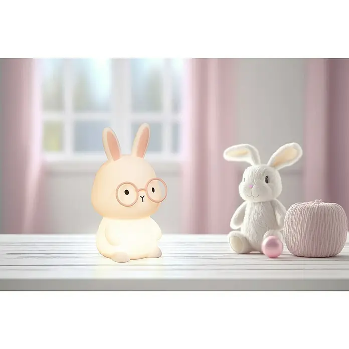 FHL easy LED-Nachtlicht Josie - 0,4 W, L x B x H: 9 x 9 x 16,3 cm, RGBW, Hase Josie - Niedliche Häschen-Nachtlampe mit Brille neben einem Plüschtier und einem rosa Wollknäuel, die eine sanfte und beruhigende Atmosphäre schaffen.