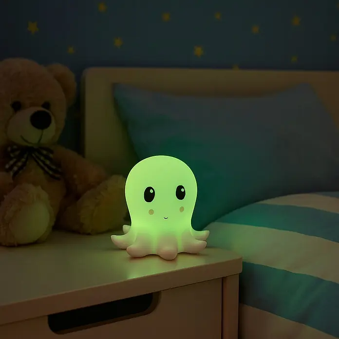 FHL easy LED-Nachtlicht Nelly - 0,4 W, L x B x H: 13,5 x 13,5 x 12 cm, RGBW, Tintenfisch Nelly - Niedliches, leuchtendes Oktopus-Nachtlicht auf einem Nachttisch neben einem Teddybär.
