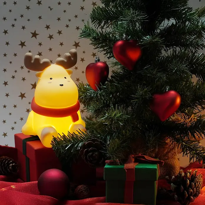 FHL easy LED-Nachtlicht Micha - 0,4 W, L x B x H: 11 x 12 x 15,5 cm, Warmweiß, Rentier Micha - Niedliches Elch-Nachtlicht auf einem Geschenk neben einem Weihnachtsbaum mit herzförmigen Ornamenten.