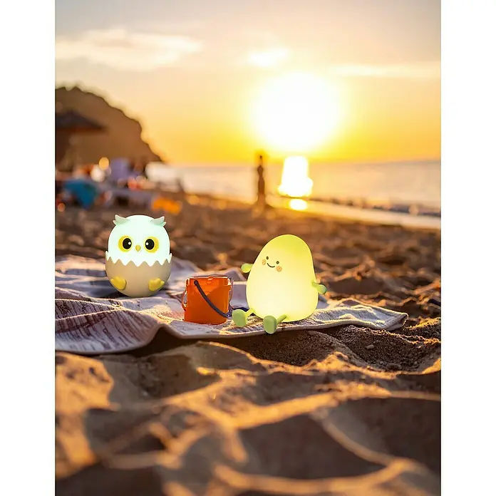 FHL easy LED-Nachtlicht Ella - 0,8 W, L x B x H: 11,5 x 9,5 x 12 cm, RGBW, Küken Ella - Niedliche LED-Nachtlichter in Eulen- und Birnenform mit Eimer auf einem Strandtuch am Strand bei Sonnenuntergang.
