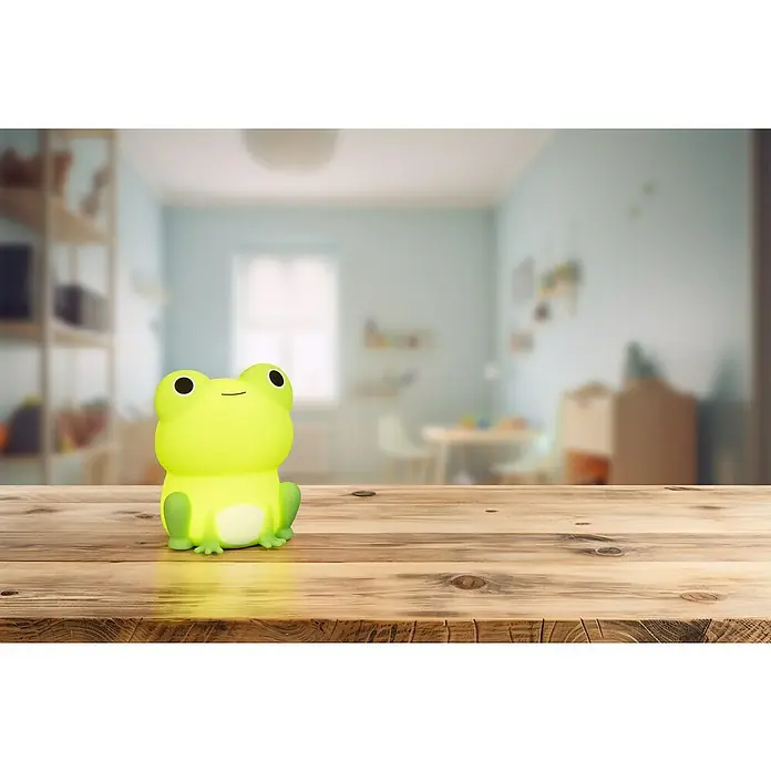 FHL easy LED-Nachtlicht Willi - 0,4 W, L x B x H: 9 x 8 x 11,5 cm, RGBW, Frosch Willi - Ein leuchtendes Frosch-Nachtlicht sitzt auf einem Holztisch und erhellt ein Kinderzimmer mit seinem sanften Schein.