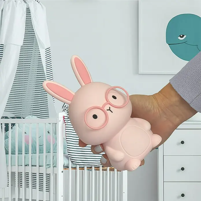 FHL easy LED-Nachtlicht Josie - 0,4 W, L x B x H: 9 x 9 x 16,3 cm, RGBW, Hase Josie - Nahaufnahme eines rosa Hasen Nachtlichts mit Brille, das in einem Kinderzimmer gehalten wird.