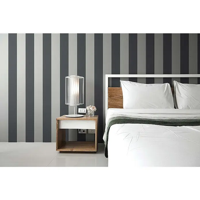 Tadessi Vliestapete M1-No.12 - Grau, Streifen, 10,05 x 0,53 m - Modernes Schlafzimmer mit weißem Bett, Holz-Kopfteil, Nachttisch aus hellem Holz und weißer Lampe vor grau-weiß gestreifter Tapete.
