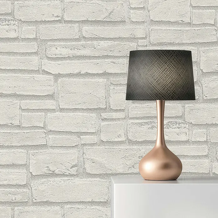 Tadessi Vliestapete M1-No.847 - Grau, Steinoptik, 10,05 x 0,53 m - Eine Tischlampe mit einem roségoldenen Fuß und einem dunkelgrau gemusterten Lampenschirm steht auf einer weißen Oberfläche.