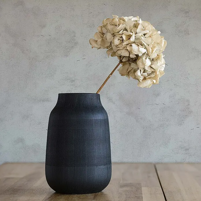 Tadessi Vliestapete M1-No.493 - Weiß, Sonstiges, 10,05 x 0,53 m - Mattschwarze Vase mit gerippten und Gitter-Texturen, die eine Trockenblume hält.