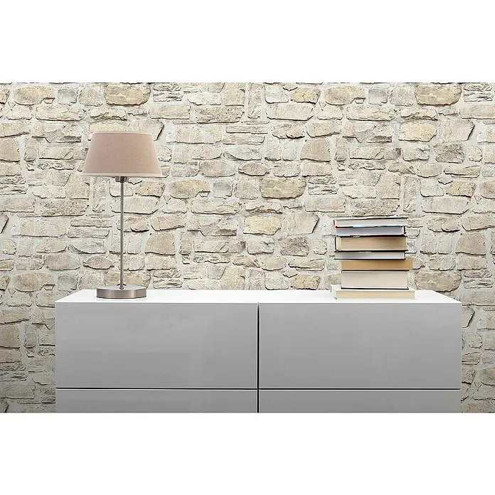 Tadessi Vliestapete M1-No.9 - Grau, Steinoptik, 10,05 x 0,53 m - Weißes, modernes Sideboard mit einer Lampe und Büchern darauf, vor einer Steinwand.