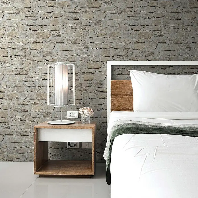 Tadessi Vliestapete M1-No.9 - Grau, Steinoptik, 10,05 x 0,53 m - Nachttisch aus Holz mit weißem offenem Regal und offener unterer Ablage, neben einem Bett, mit weißer Lampe und Blumen.