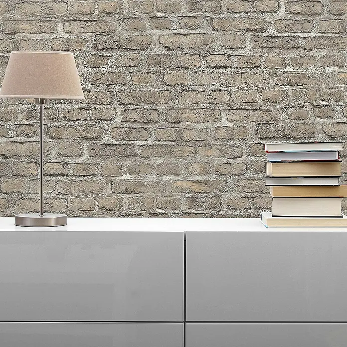Tadessi Vliestapete M1-No.160 - Grau, Steinoptik, 10,05 x 0,53 m - Strukturierte Ziegelwand in Grautönen, als stilvolle Kulisse in einem Raum mit Lampe und Büchern.