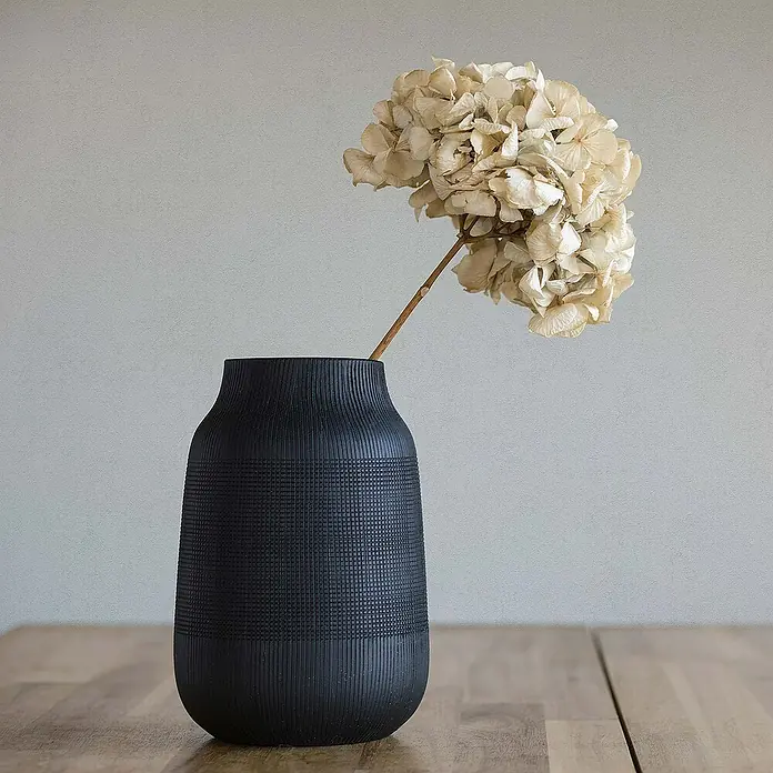 Tadessi Vliestapete M1-No.587 - Weiß, Steinoptik, 10,05 x 0,53 m - Schwarze strukturierte Vase mit geripptem und kariertem Muster, hält getrocknete helle Hortensien auf einem Holztisch.