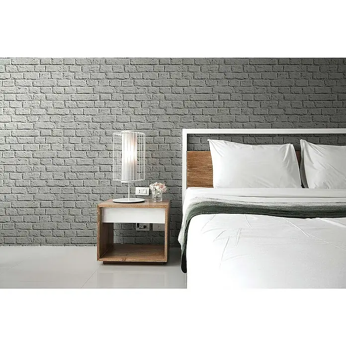 Tadessi Vliestapete M1-No.271 - Grau, Steinoptik, 10,05 x 0,53 m - Modernes Schlafzimmer mit weißem Bett, Nachttisch aus Holz und weißer Lampe vor einer grauen Ziegelwand.