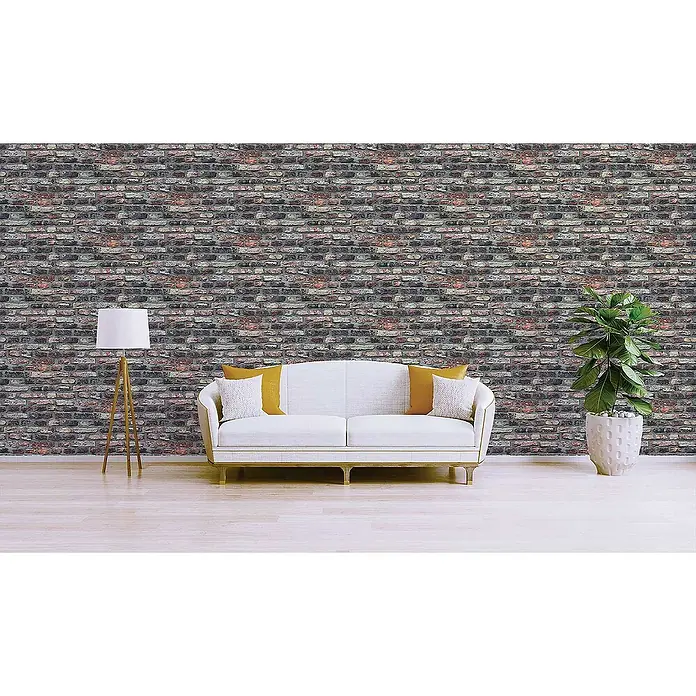 Tadessi Vliestapete M1-No.2661 - Grau, Steinoptik, 10,05 x 0,53 m - Rustikale, verwitterte Ziegelwandtapete in einem Raum mit weißem Sofa, Lampe und Pflanze, die ihr dunkles, mehrfarbiges Design zeigt.