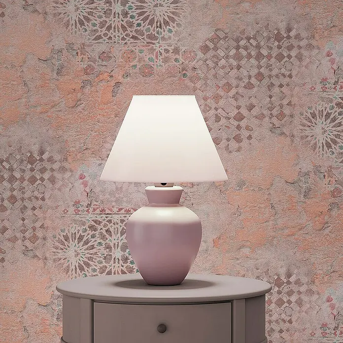 Tadessi Vliestapete M1-No.605 - Orange, Fliesenoptik, 10,05 x 0,53 m - Eine pinkfarbene Tischlampe mit weißem Schirm steht auf einem grauen Nachttisch und beleuchtet eine strukturierte Wand mit abstrakten Mustern.