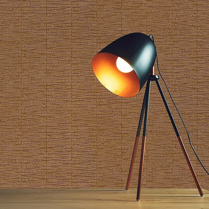 Tadessi Vliestapete M1-No.1709 - Orange, Sonstiges, 10,05 x 0,53 m - Eine schwarze und kupferfarbene Dreibeinlampe mit beleuchteter Birne, die ein warmes Licht auf einen Holzboden vor einer strukturierten Wand wirft.