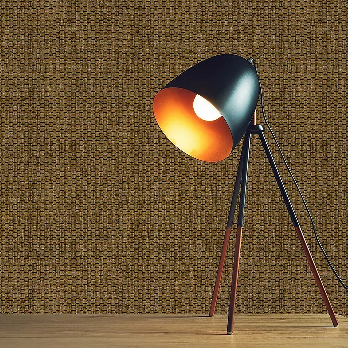 Tadessi Vliestapete M1-No.1731 - Schwarz, Sonstiges, 10,05 x 0,53 m - Eine schwarze Dreibeinlampe mit orangefarbenem Innenraum und Holzbeinen spendet warmes Licht auf einem Holztisch vor einer texturierten goldbraunen Wand.