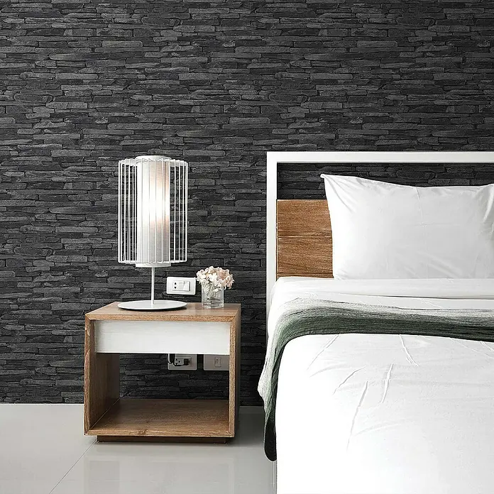 Tadessi Vliestapete M1-No.2 - Schwarz, Steinoptik, 10,05 x 0,53 m - Moderner Nachttisch aus Holz mit weißer Schublade, neben einem Bett, mit weißer Lampe und kleinem Blumenstrauß.