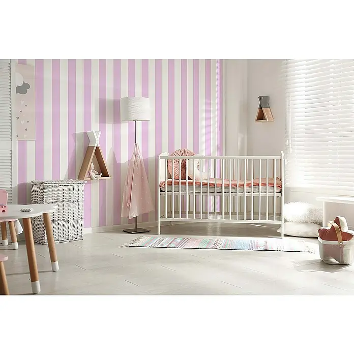 Tadessi Vliestapete M1-No.767 - Rosa, Streifen, 10,05 x 0,53 m - Ein gemütliches Kinderzimmer mit rosa-weiß gestreifter Tapete, einem weißen Babybett und einer Stehlampe.