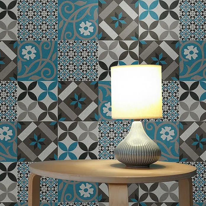 Tadessi Vliestapete M1-No.522 - Schwarz, Fliesenoptik, 10,05 x 0,53 m - Gemusterte Wandverkleidung mit blauen, grauen und schwarzen geometrischen und floralen Designs, hinter einem Tisch und einer Lampe.