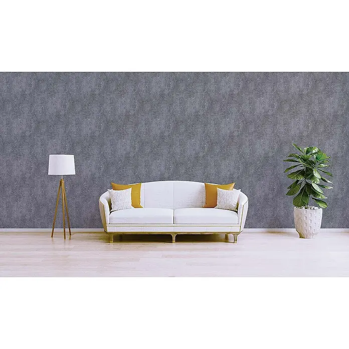 Tadessi Vliestapete M1-No.585 - Grau, Steinoptik, 10,05 x 0,53 m - Graue, strukturierte Tapete an einer Wohnzimmerwand hinter einem weißen Sofa, einer Lampe und einer Pflanze.